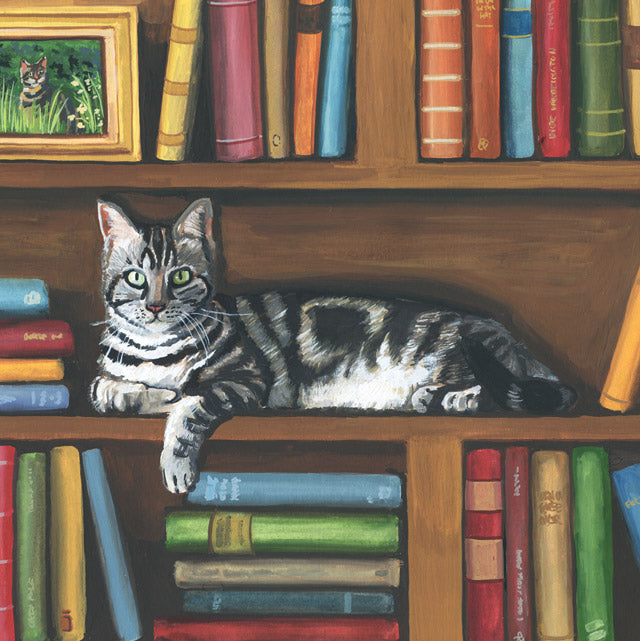 A painted scene of a gray tabby cat lying on a wooden bookshelf surrounded by colorful books. A small framed picture of a cat appears in the upper left corner.