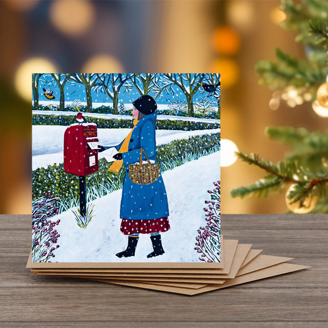 Christmas card by Marcella Cooper with a woman posting a letter in the snow, surrounded by festive decorations.