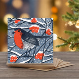 A square winter greeting card featuring a red-breasted robin, blue-gray background, and red berries.